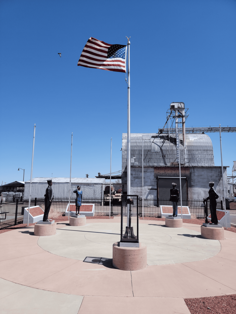 American flag with military statues in outdoor plaza.