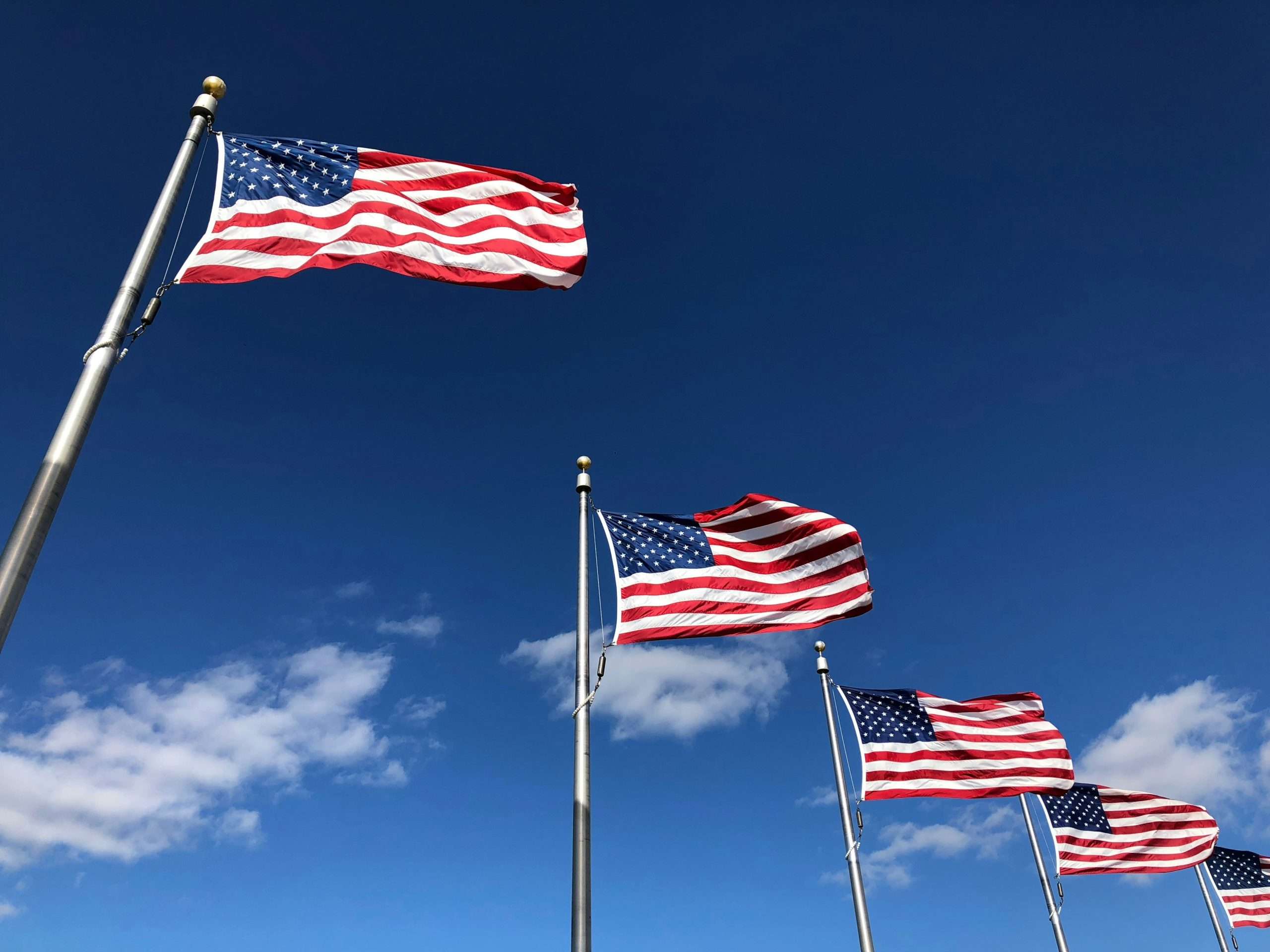 Five American flags waving against a blue sky