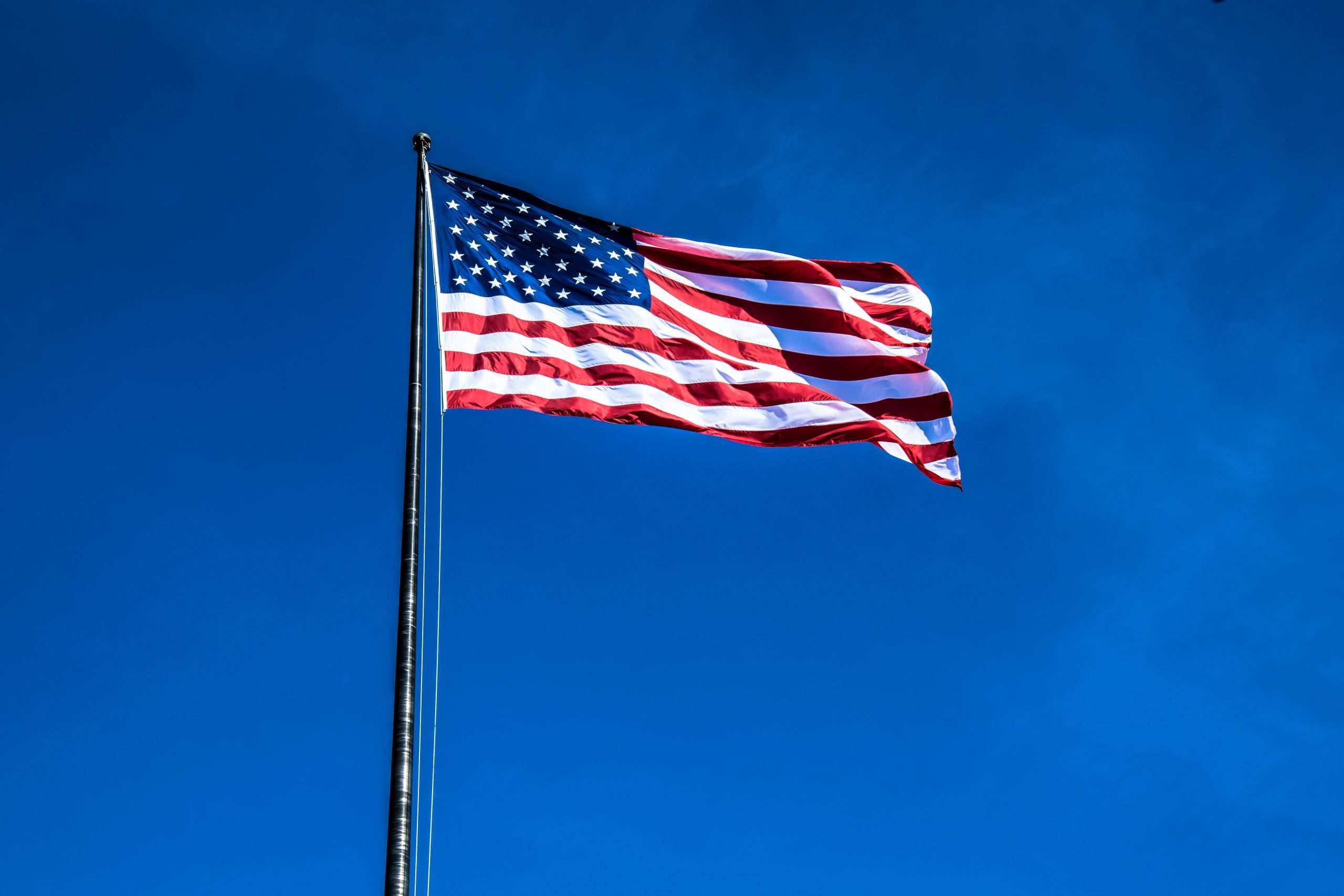 American flag waving against clear blue sky.