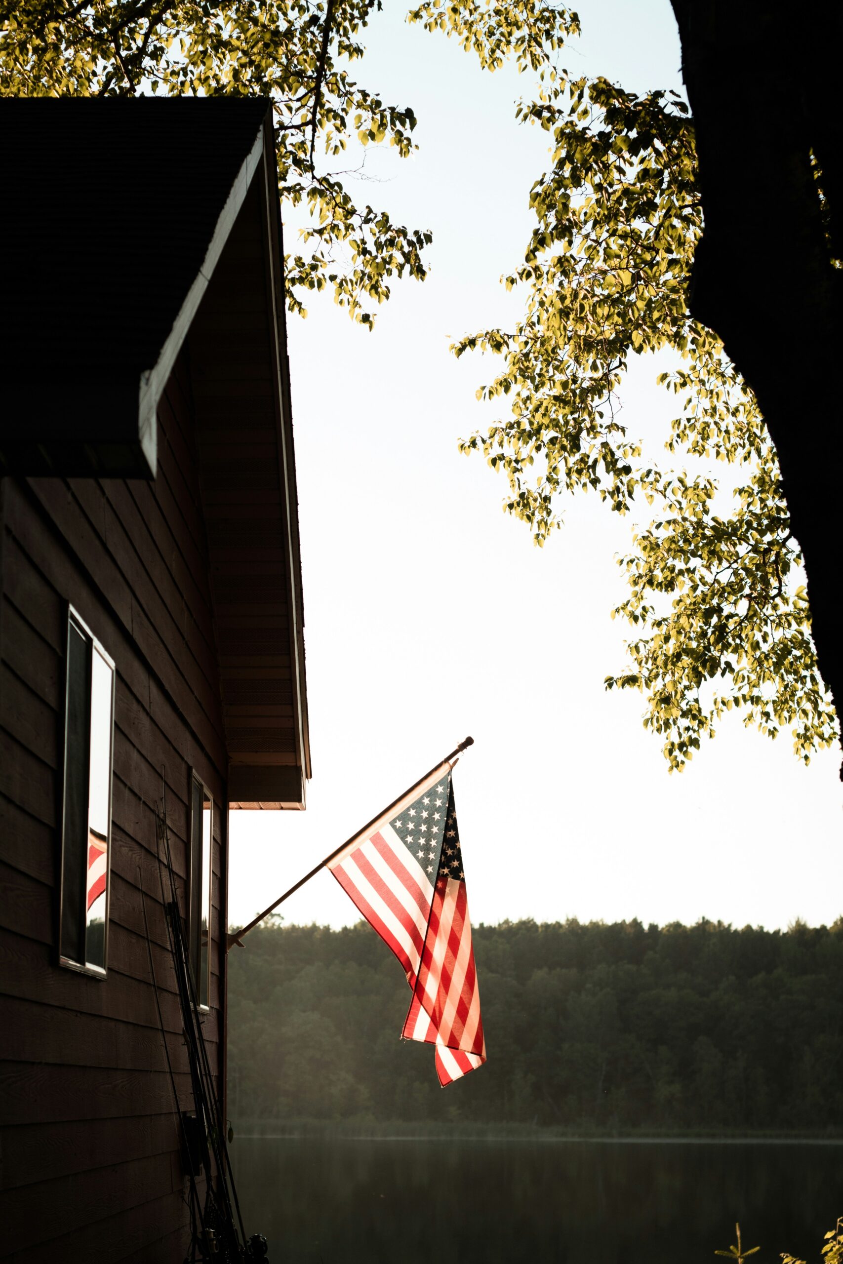American flag on cabin by lake and trees.