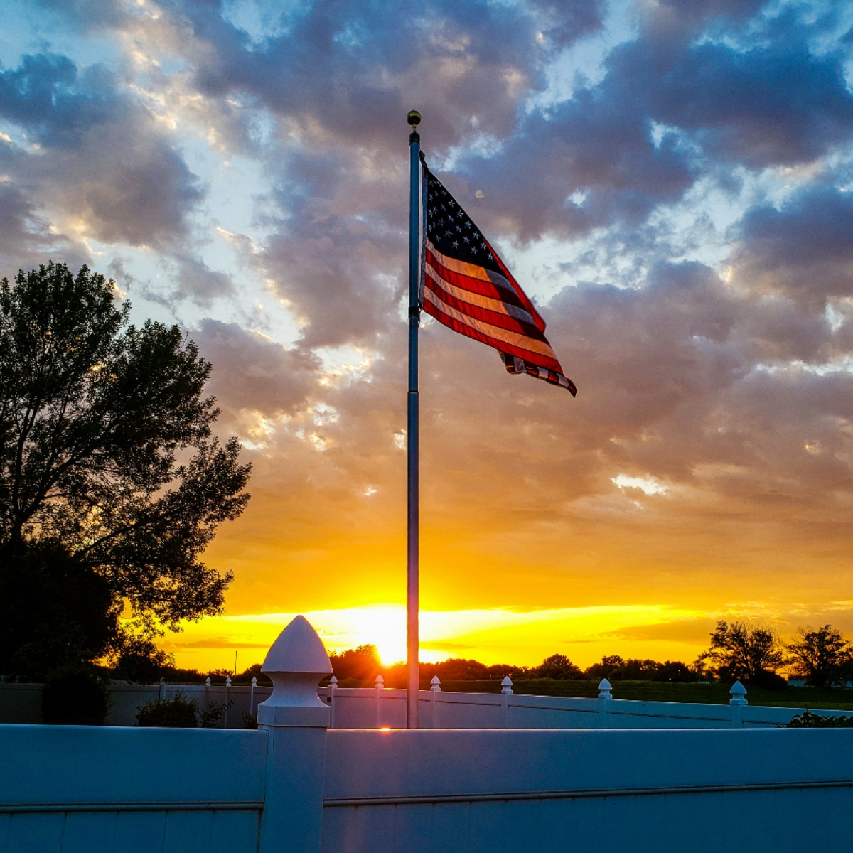 American flag waving at sunset with cloudy sky.