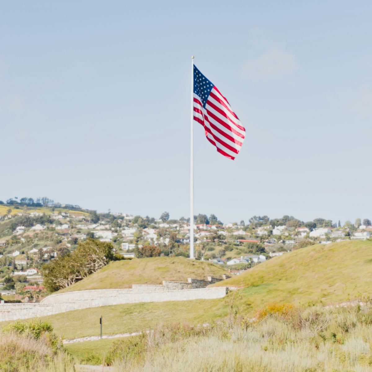 American flag on hill with houses in background.