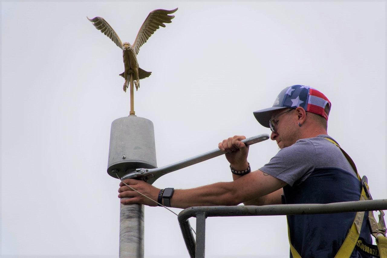 flgplinst Worker adjusts eagle-topped flagpole from elevated platform
